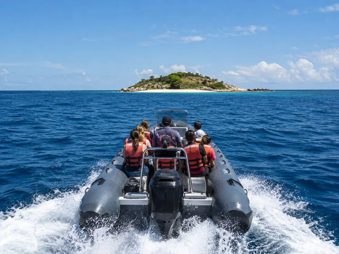 Ein schnelles Schlauchboot mit Passagieren, das über offenes, blaues Wasser auf eine kleine sichelförmige Insel zufährt