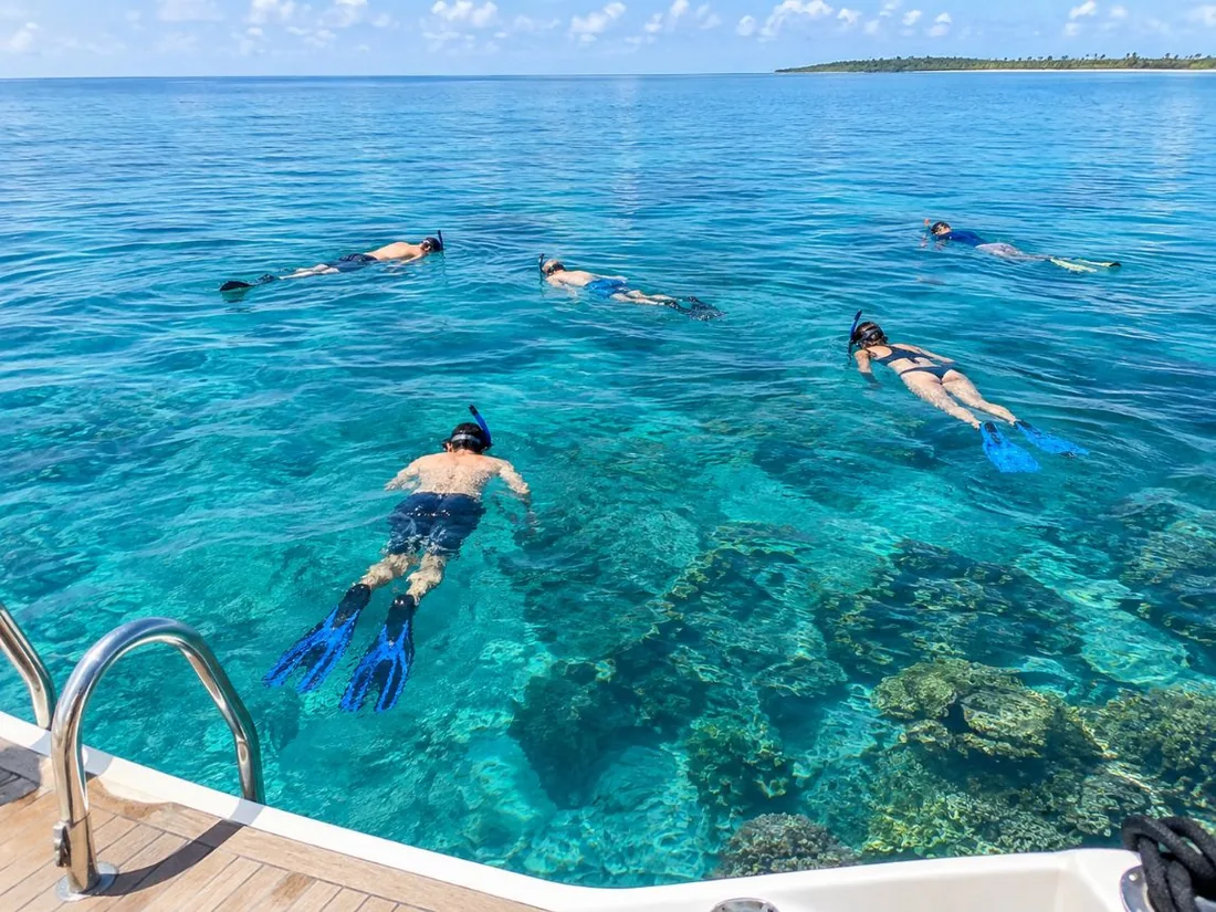 Snorkelistas flotando boca abajo en aguas turquesas tranquilas y claras, vistos desde un barco